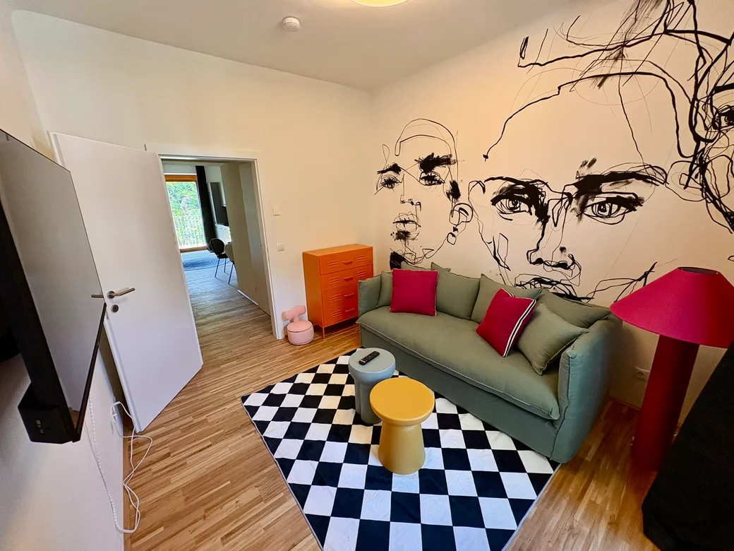 Wohnzimmer mit Gesichter-Wandbild und grüner Couch – Pop Art